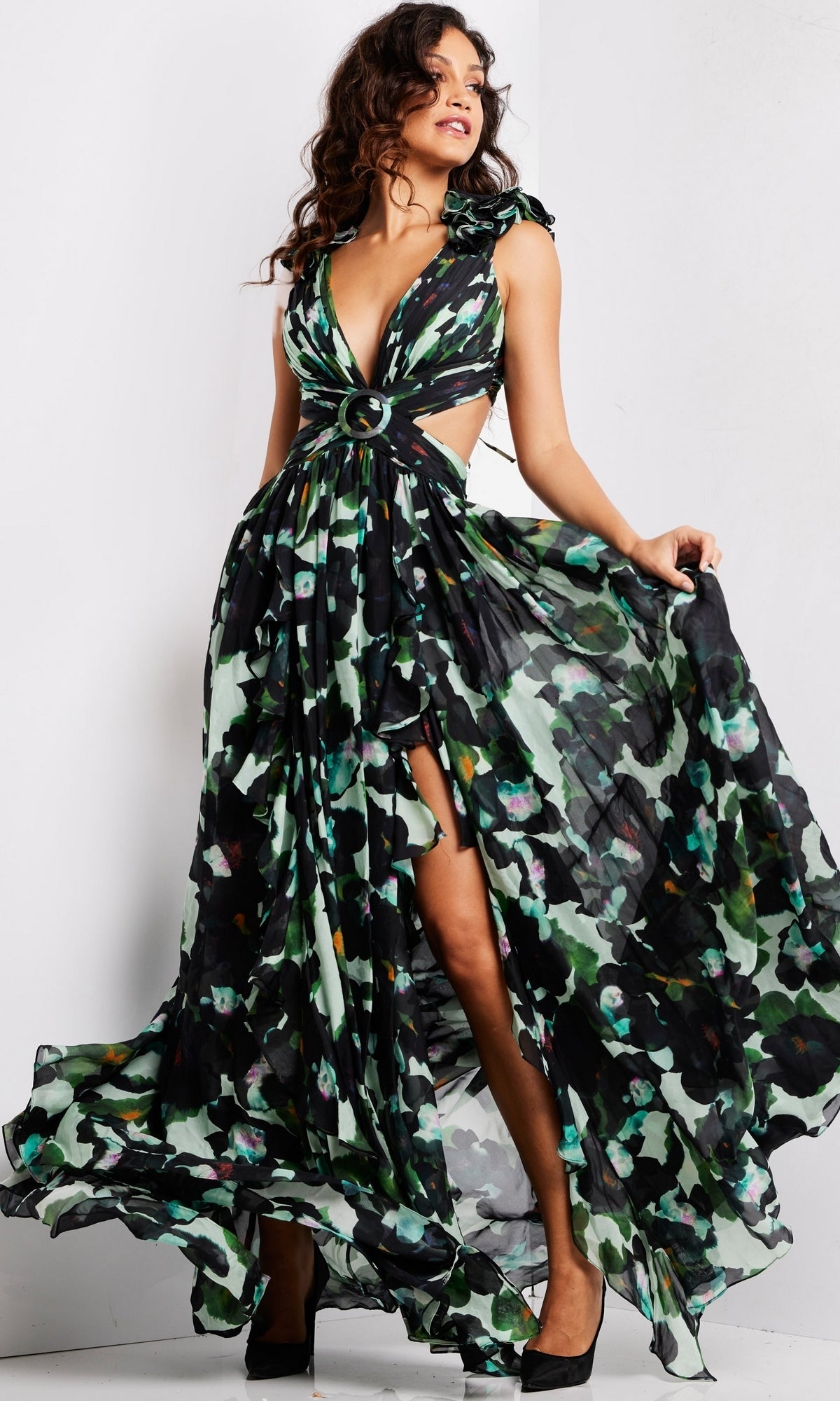 A woman poses with one leg exposed while holding the skirt of the Long Prom Dress 39420 by Jovani, a sleeveless, floor-length dark floral chiffon formal dress featuring a v-neckline, side cutouts, and a ring accent at the waist.